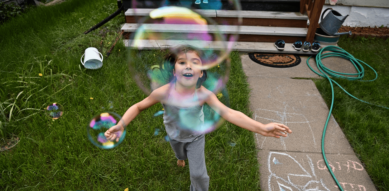 Child running through grass, surrounded by colorful bubbles.