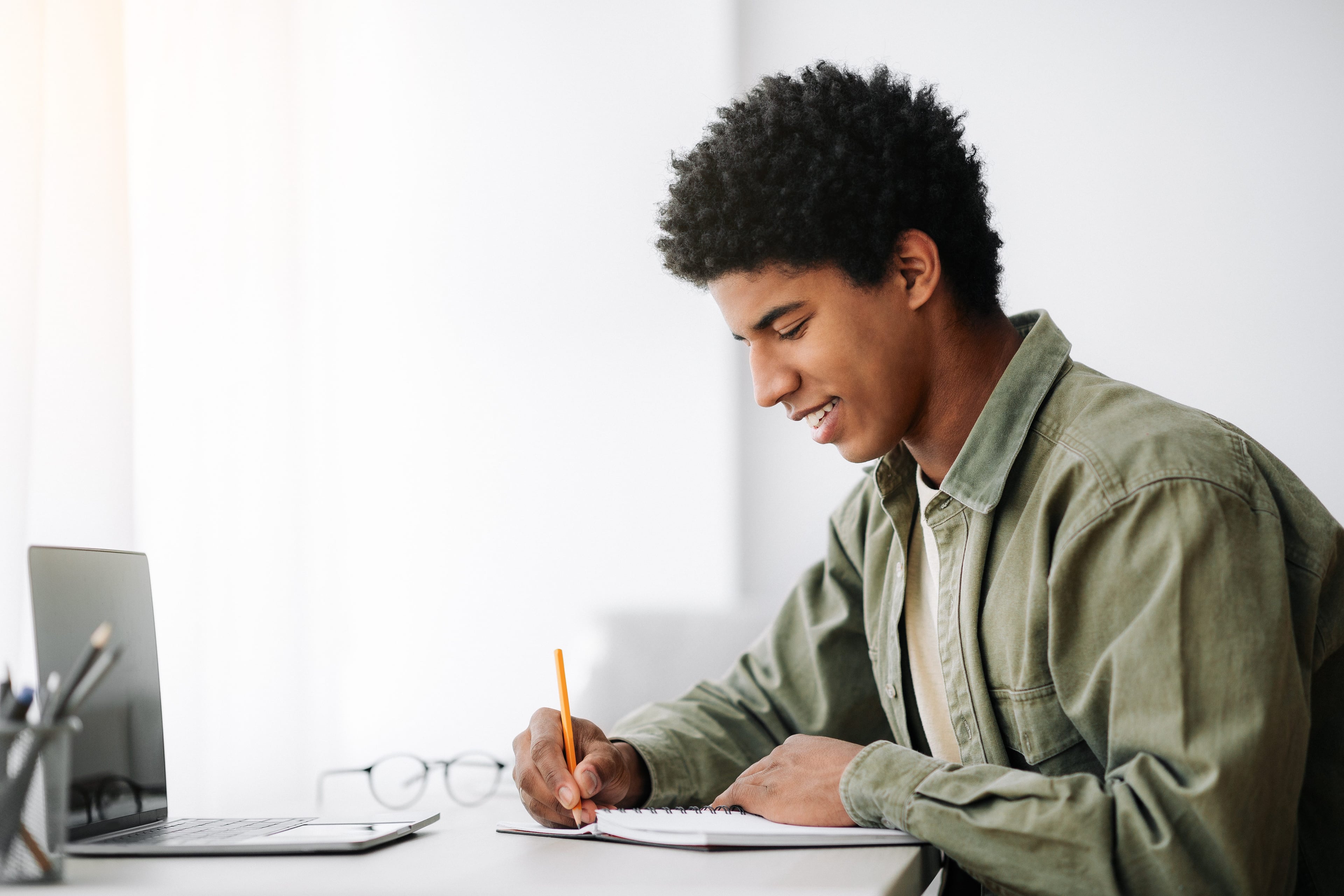 Smiling young adult writing in a notebook with a pencil.